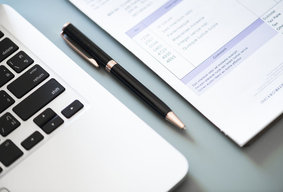 Caneta preta ao lado de um notebook e um papel de relatório.